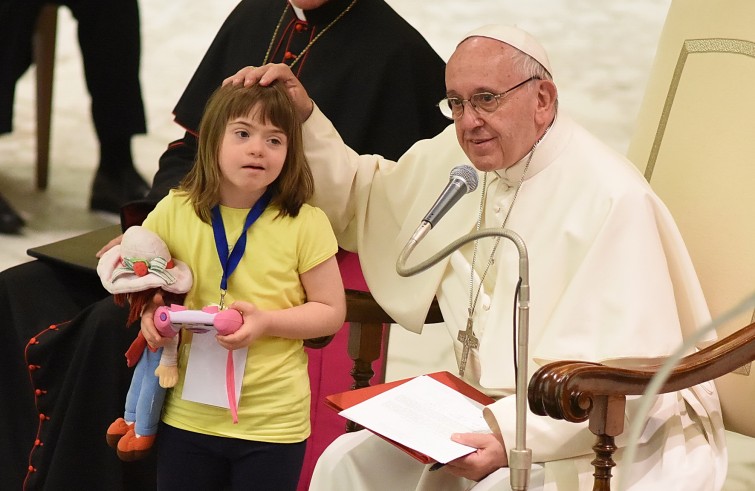 Aula Paolo VI, 11 gennaio 2016: convegno Cei per il 25° del Settore per la catechesi delle persone disabili - Papa Francesco scherza con una bambina down davanti alla poltrona